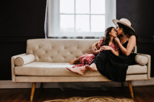 Family photographer, a mother and her daughter recline on the couch together as they spend time together, mom kisses daughter